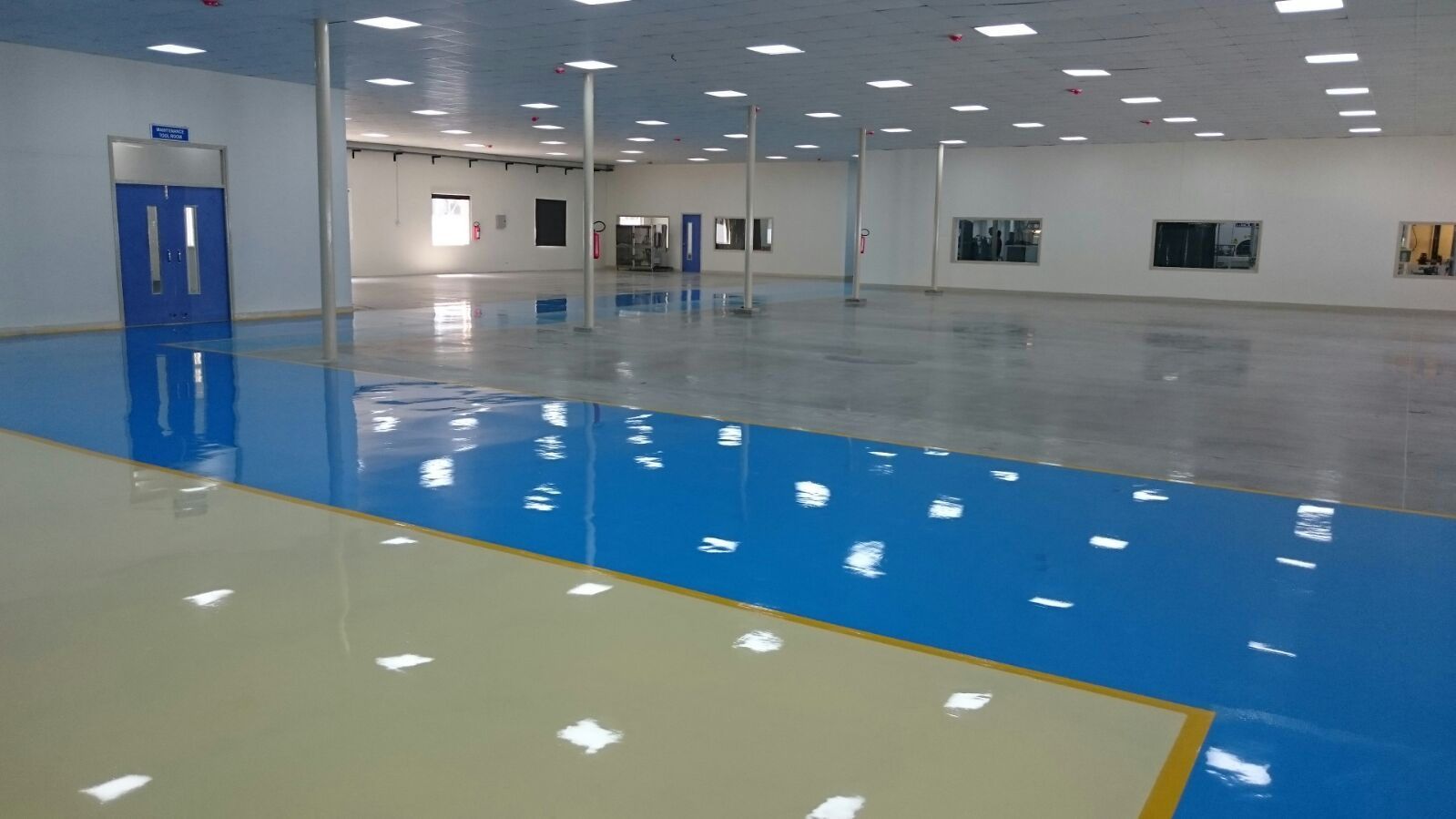 Sala industrial diáfana con revestimiento continuo de resina en azul y crema, brillante y sin juntas