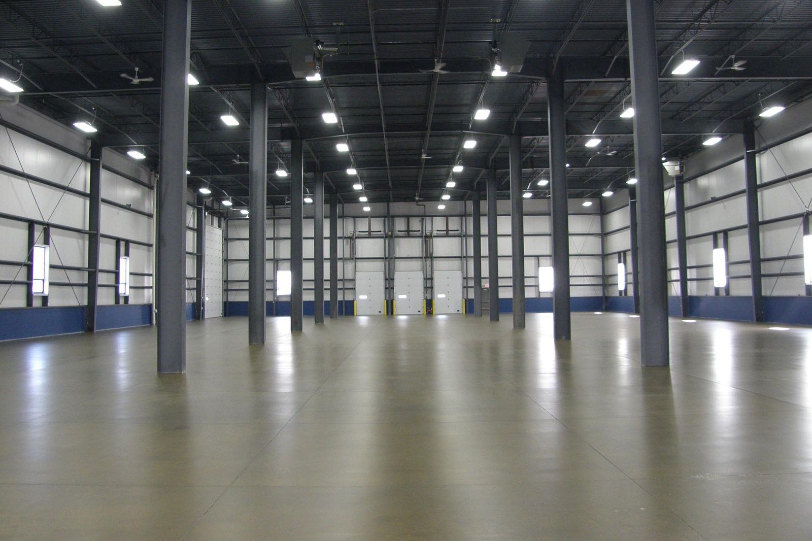 Nave industrial vacía con columnas de acero y solera pulida que refleja la iluminación cenital