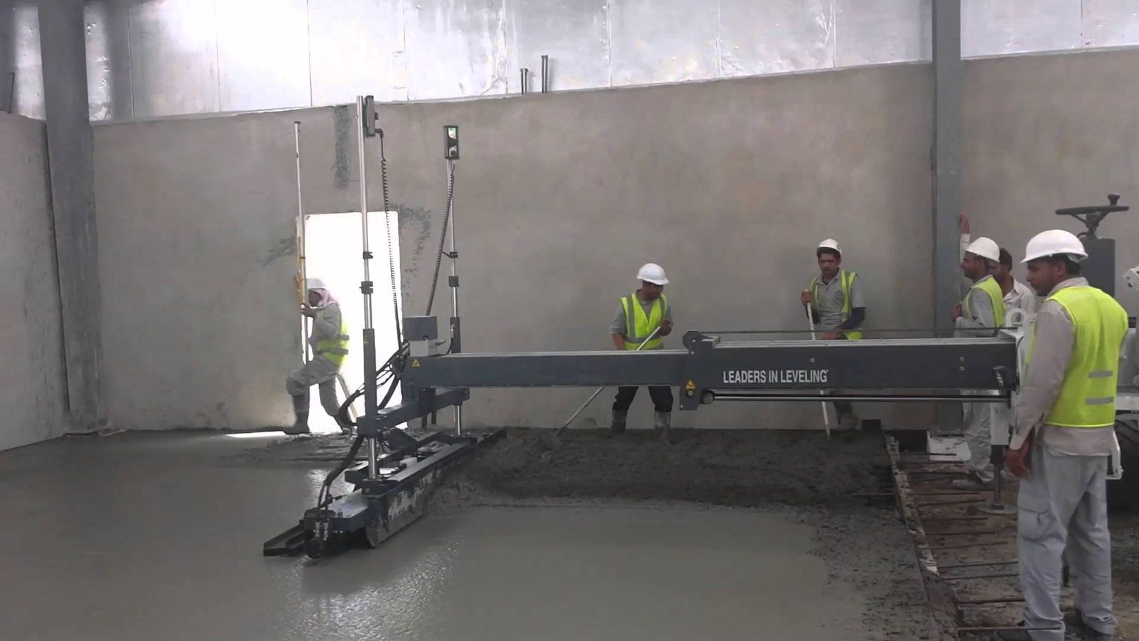 Equipo de cuatro operarios extendiendo hormigón con una laser screed en el interior de una nave