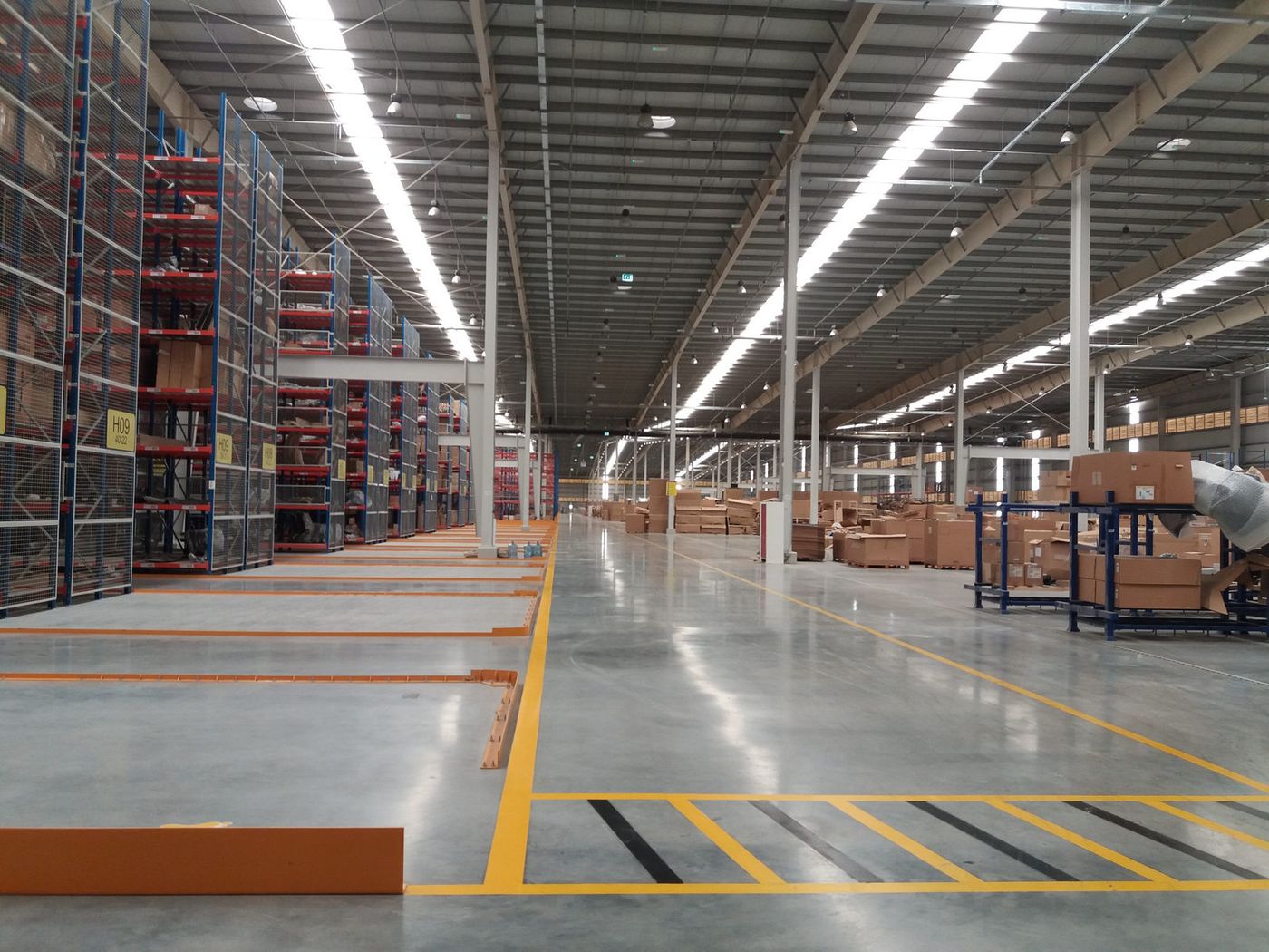 Almacén en servicio con estanterías de gran altura y solera pulida con señalización de pasillos en amarillo